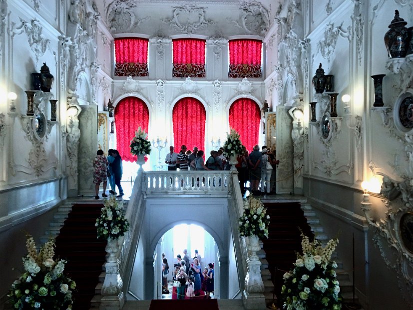 L'escalier d'honneur en marbre de Carrare : les rideaux rouges se détachent sur le fond blanc de ses murs et de ses plafonds couverts de moulures.